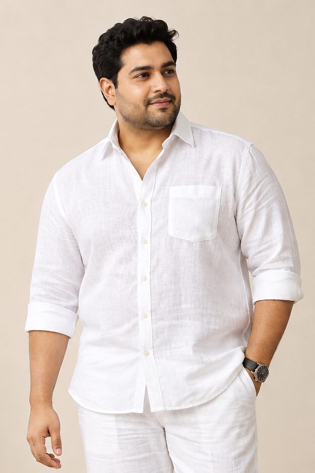 A man modeling a white two-piece linen set consisting of a long-sleeve button-up shirt and matching trousers, paired with white sneakers, against a neutral beige background.