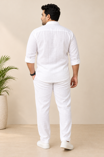 A man shown from the back wearing a white textured linen shirt and matching white trousers, standing in a studio setting with a beige background.