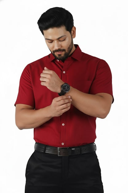 Man wearing a red shirt and black pants, adjusting his watch on a white background